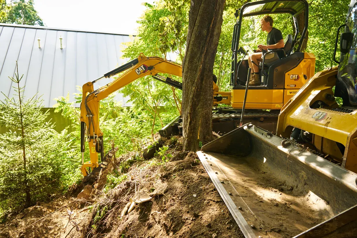 Excavator operator digging a hillside next to a loader bucket