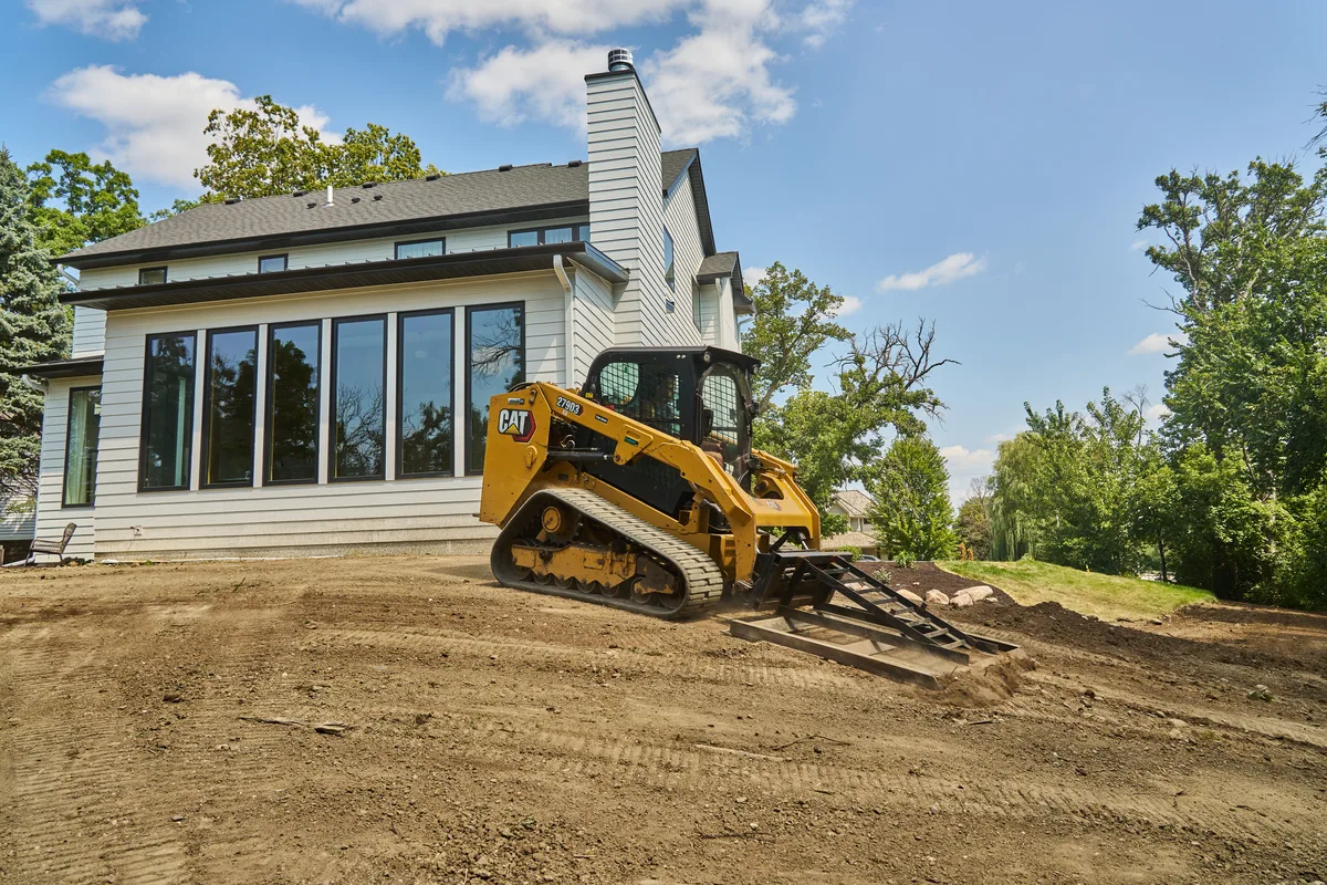 Landscape rake finishing a level graded pad behind a home