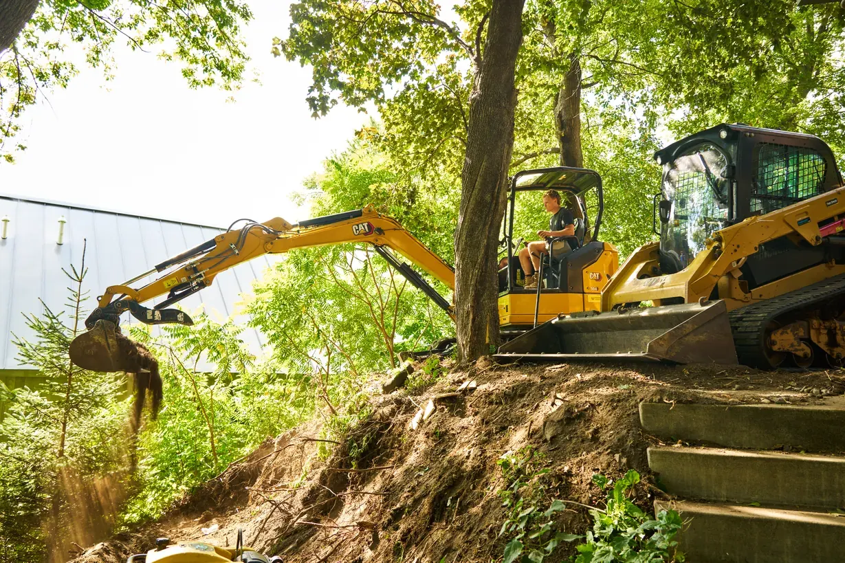 Excavator dumping soil while reshaping a hillside lot