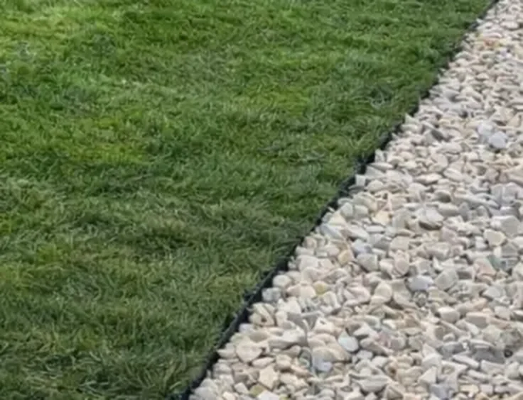 Crushed rock border held by black landscape edging beside new sod