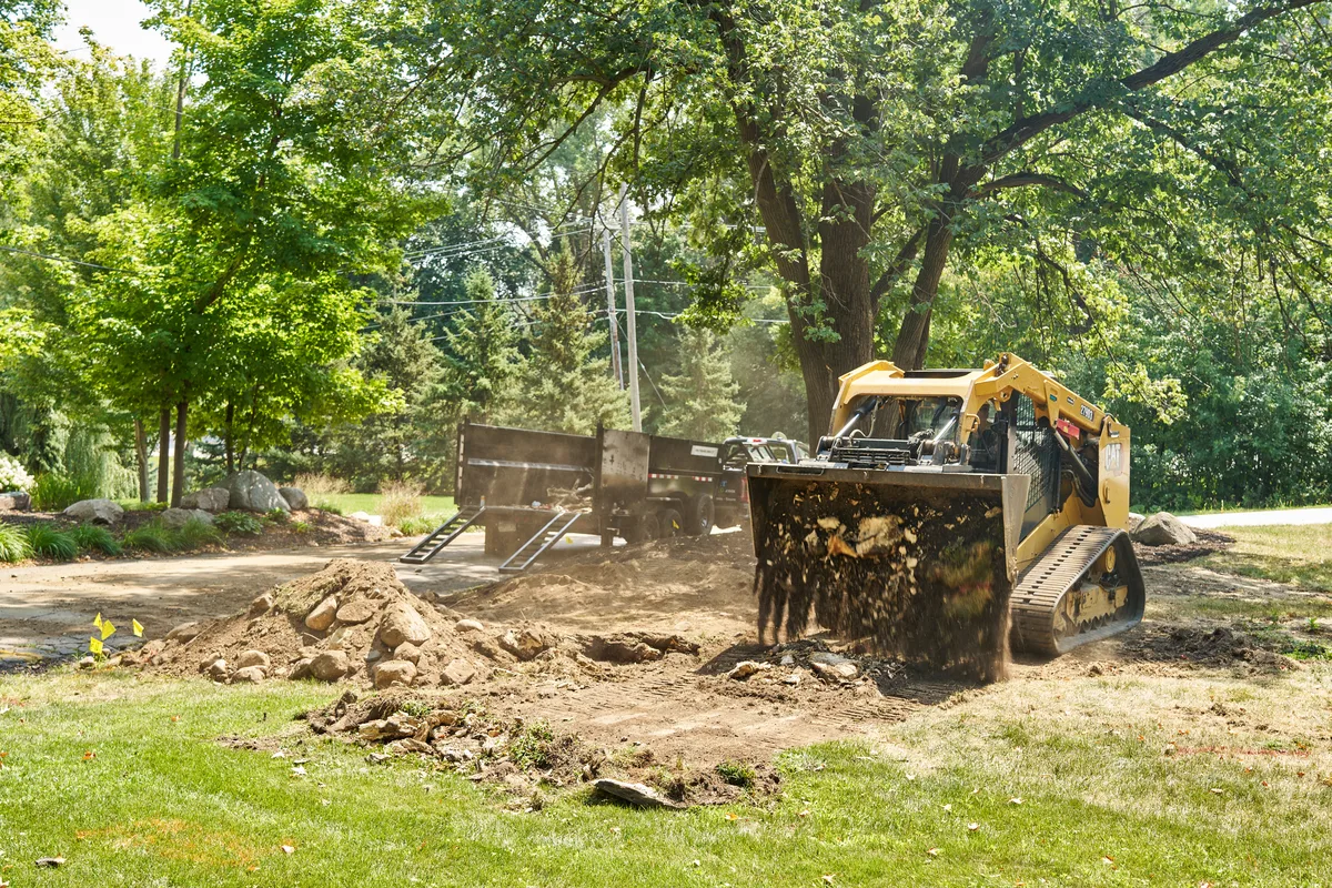 Skid steer and dump trailer removing brush, rock, and stumps from a residential lot